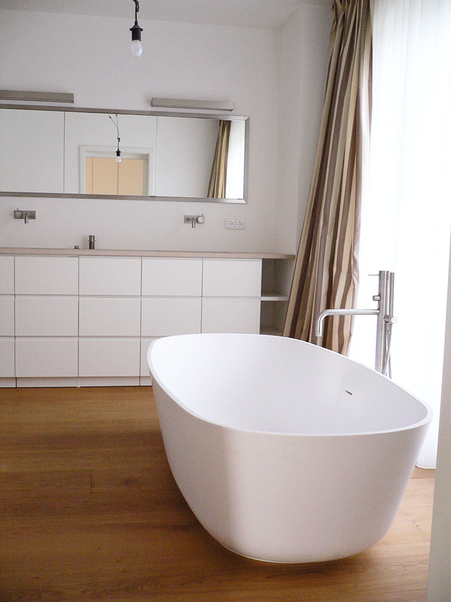 Helles Bad mit freistehender Badewanne, weißen Unterschränken und Holzboden
