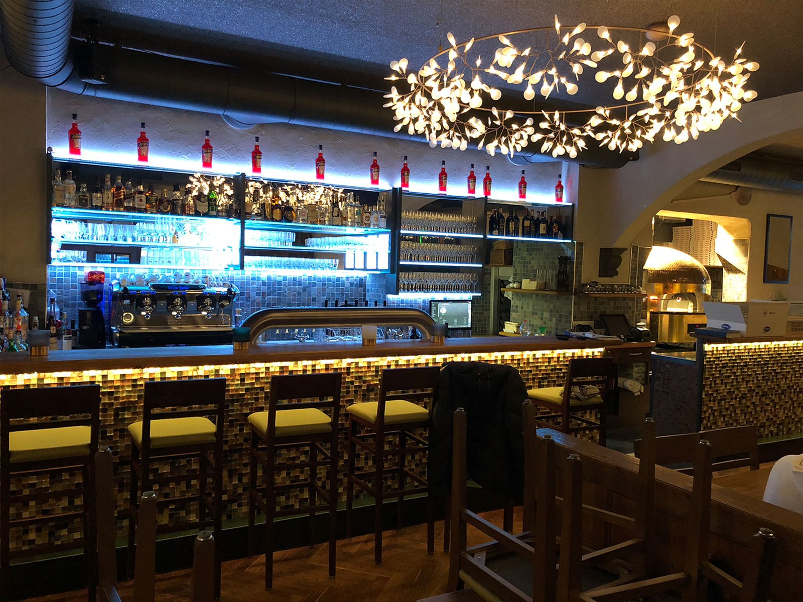 Restaurant mit beleuchteter Bar, Barhockern und einem großen Leuchter aus Blättern
